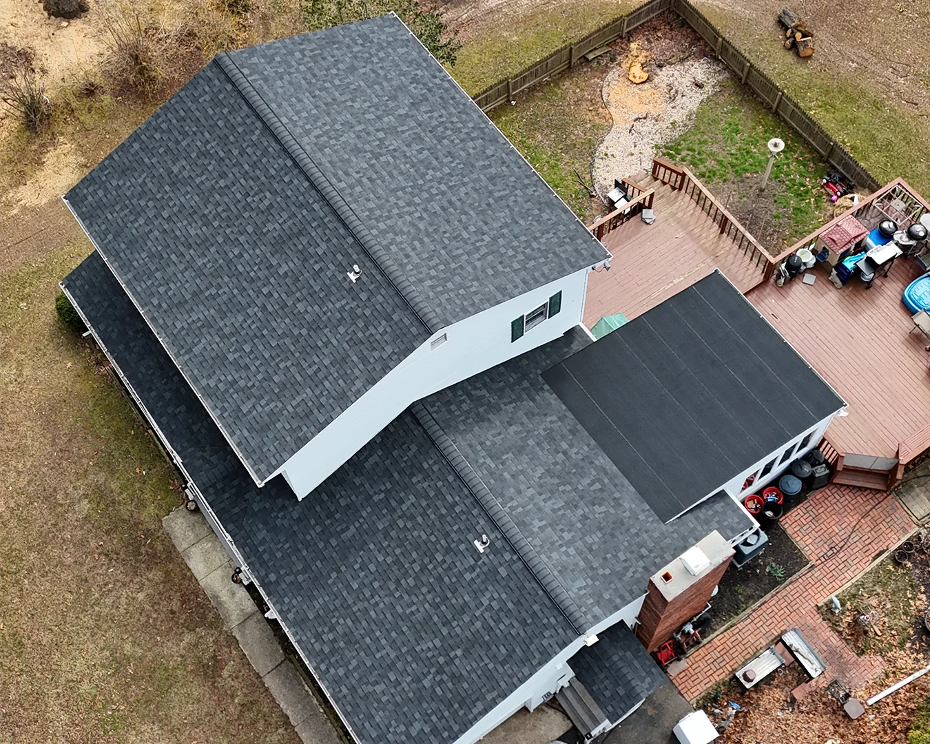 Aerial view of a house with a dark shingle roof and a backyard patio
